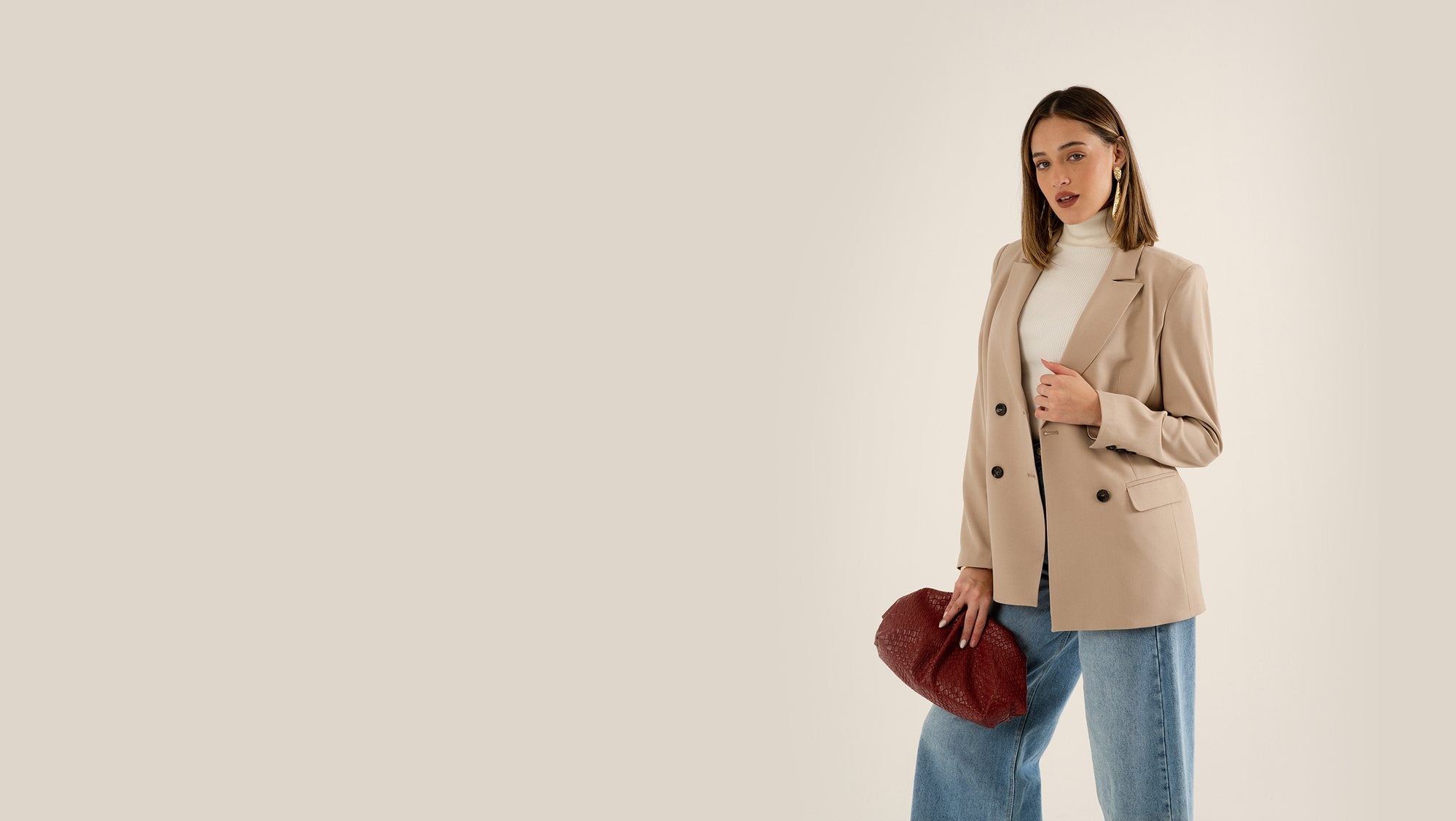 Model in a beige double-breasted blazer and wide-leg jeans holding a red clutch